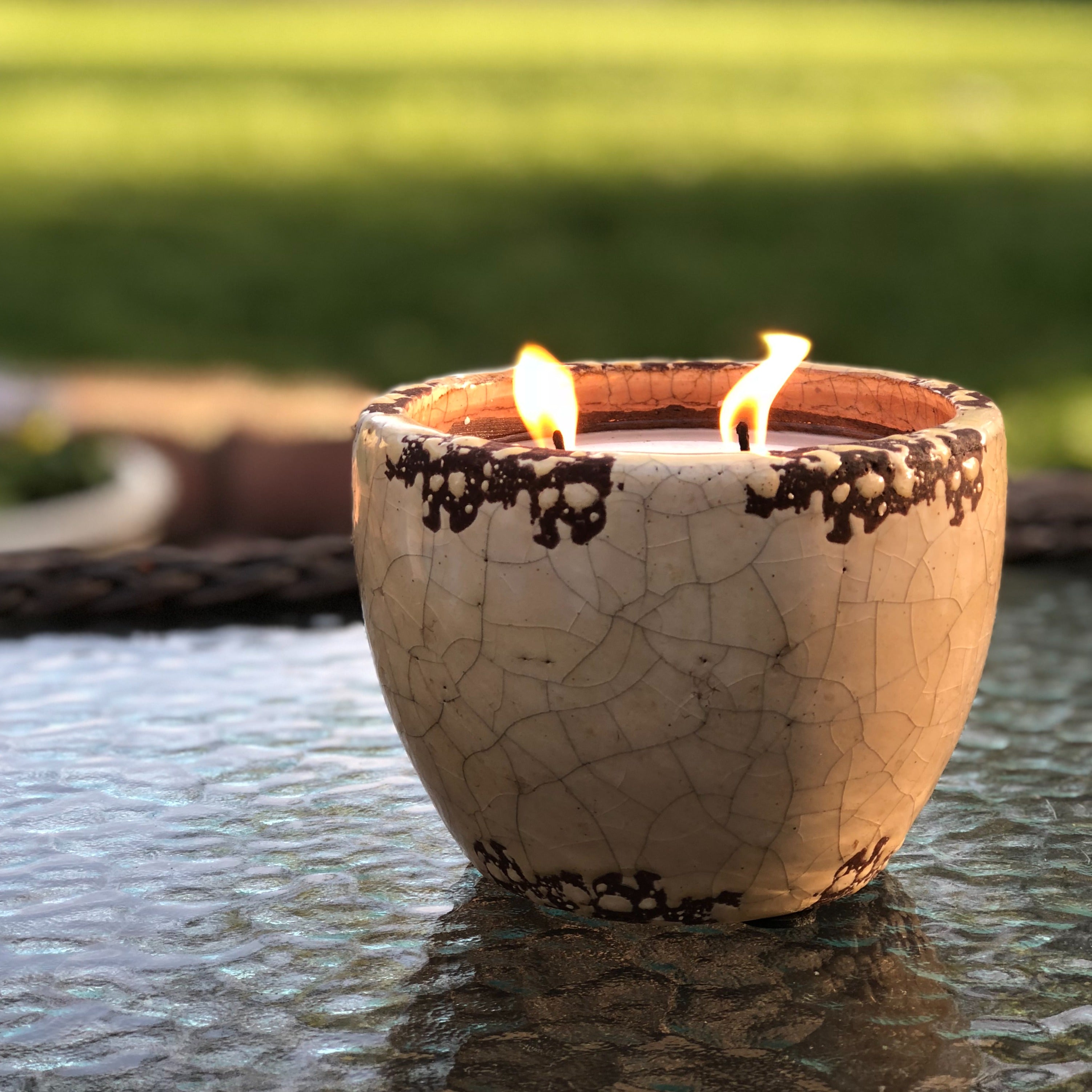 A ceramic garden candle with a double wick burning in an outdoor setting, providing a mosquito repellent function.