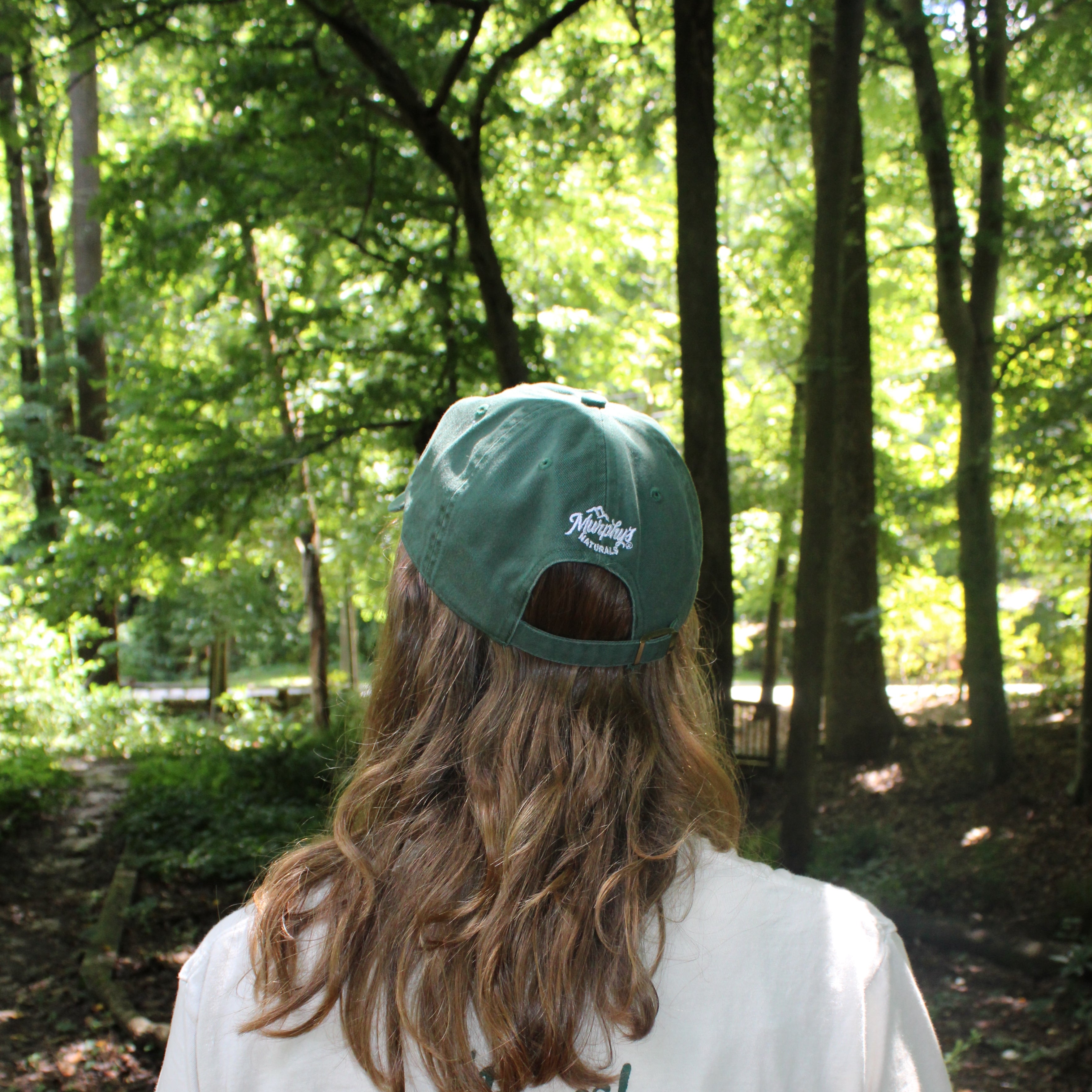 Murphy's logo on the back of a green hat. The person wearing it is in a wooded area and looking away.