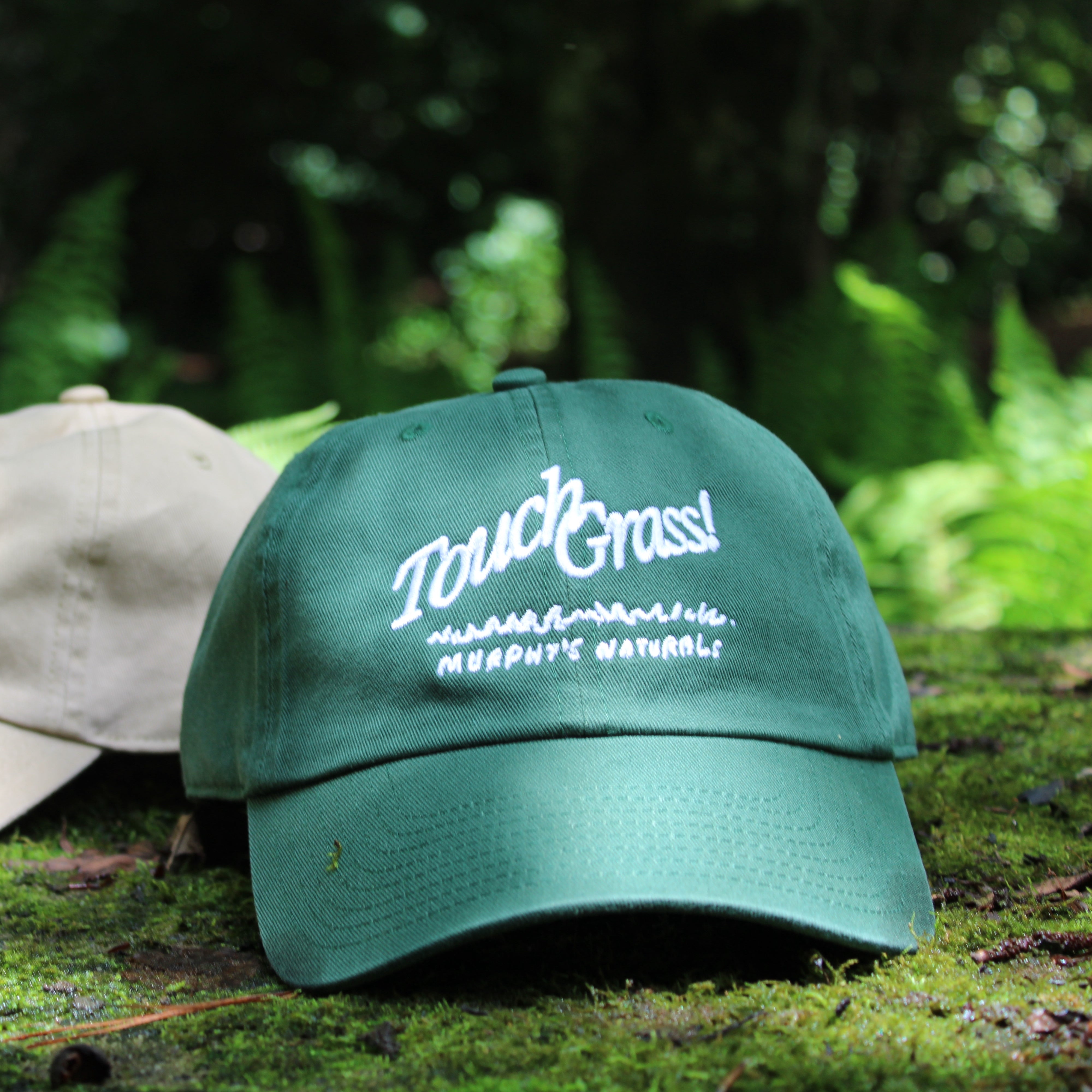 a green hat stating, "touch grass!" sitting on a mossy surface