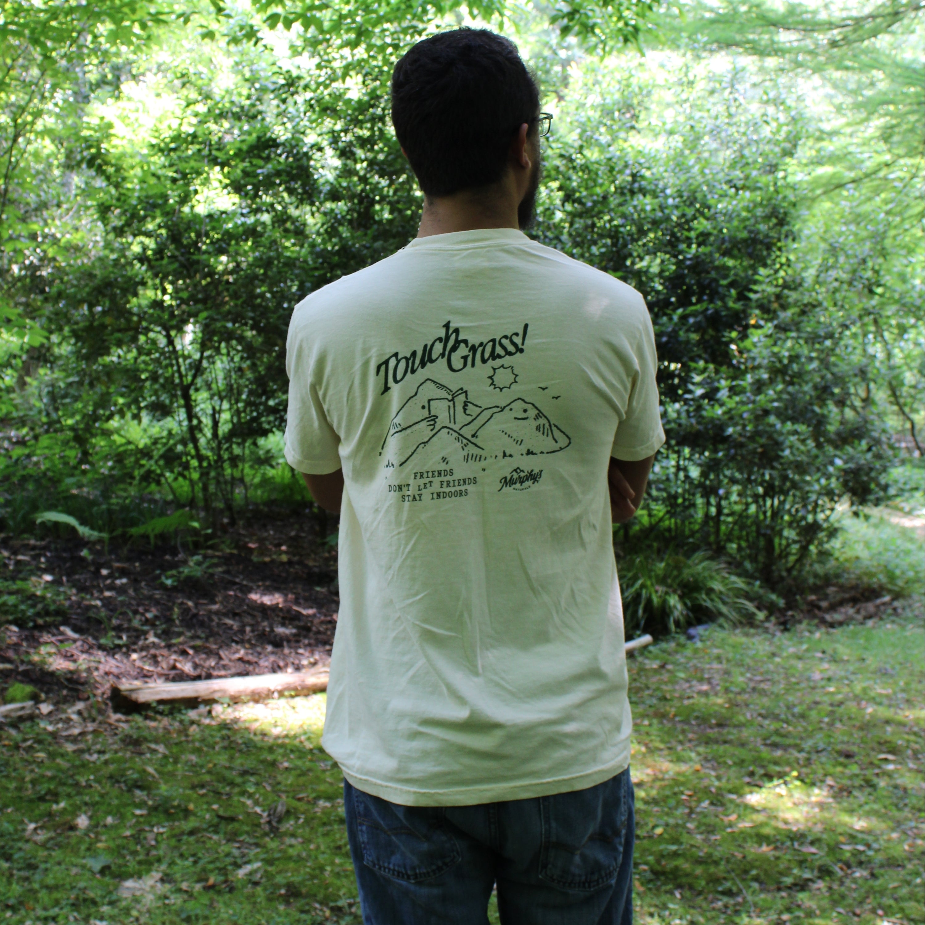 A person looking away wearing a t shirt stating, "touch grass, friends don't let friends stay indoors."