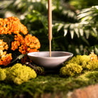 grey incense stick holder with green moss around it
