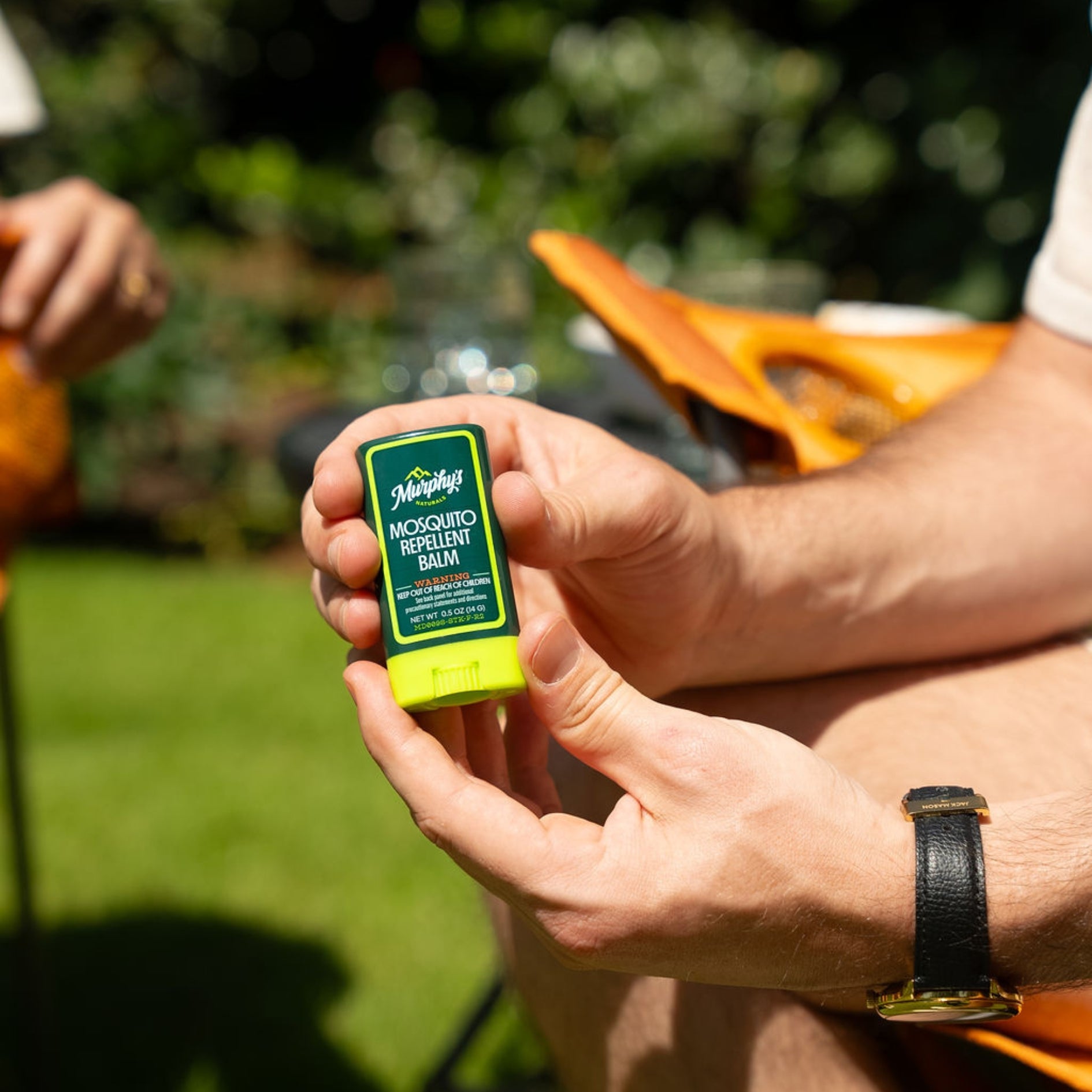 A person holding a green and bright green mosquito repellent balm stick outdoors.
