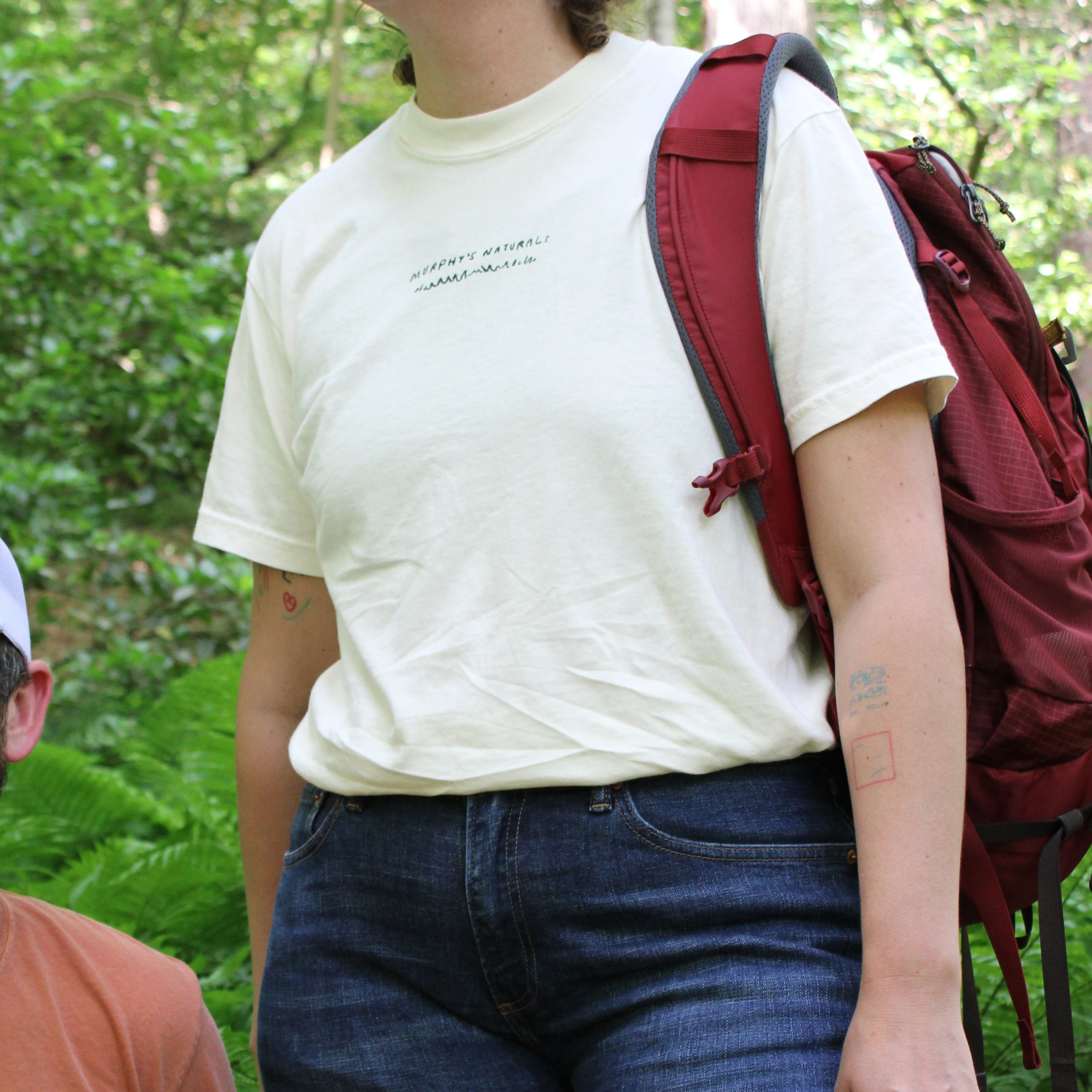 A person wearing a t shirt and a backpack slung over their shoulder.