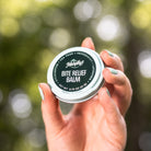 A person holding a tin container labeled 'Bite Relief Balm' with a blue and white design