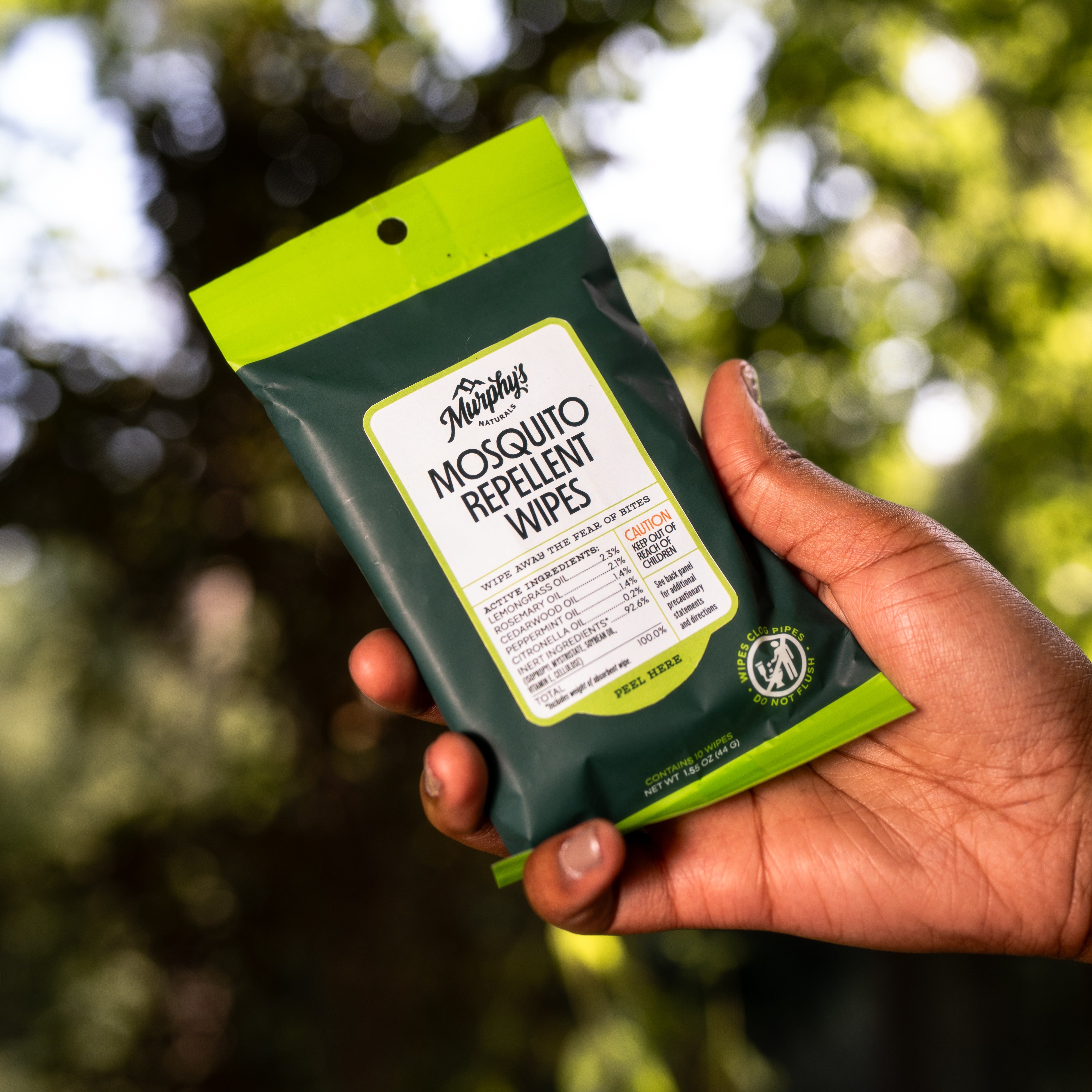 A hand holding a pack of mosquito repellent wipes with green packaging, outdoors.