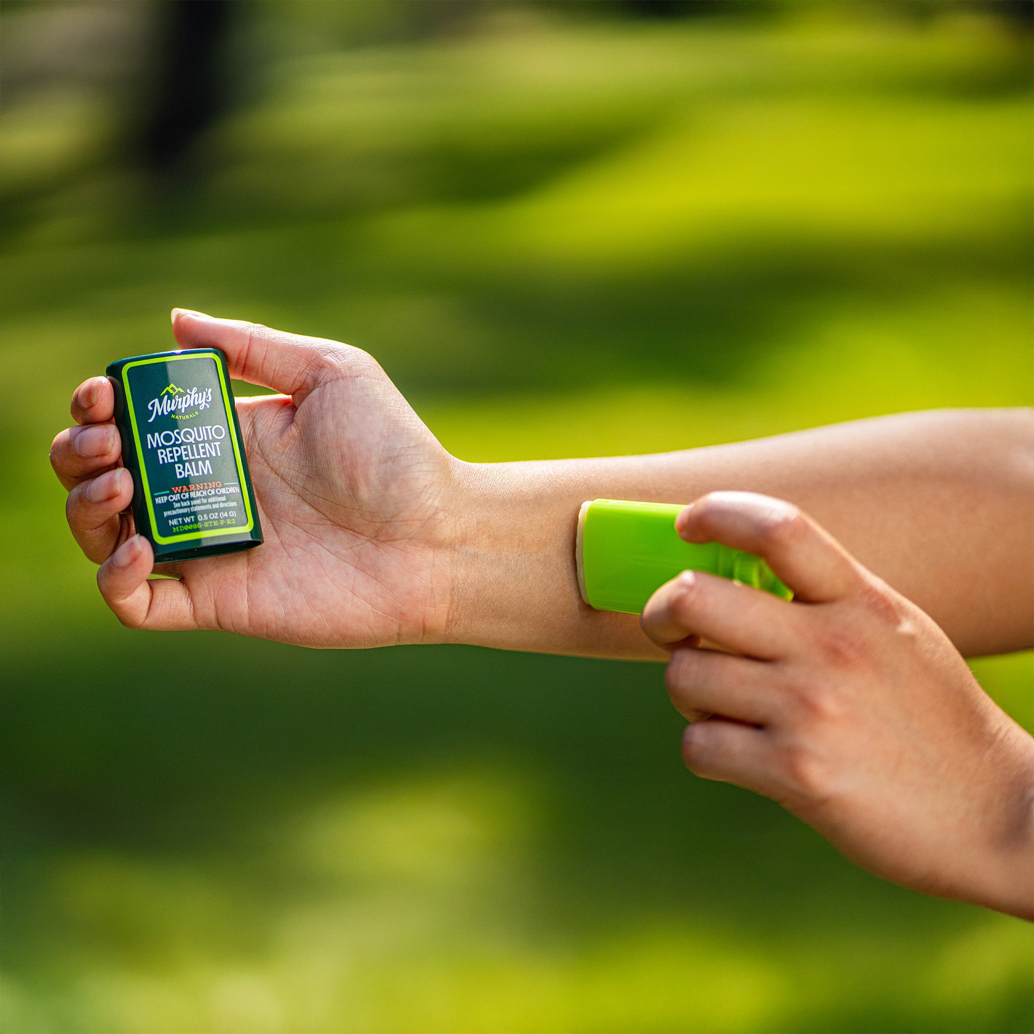 Person applying a green balm to their arm with a blurred green background