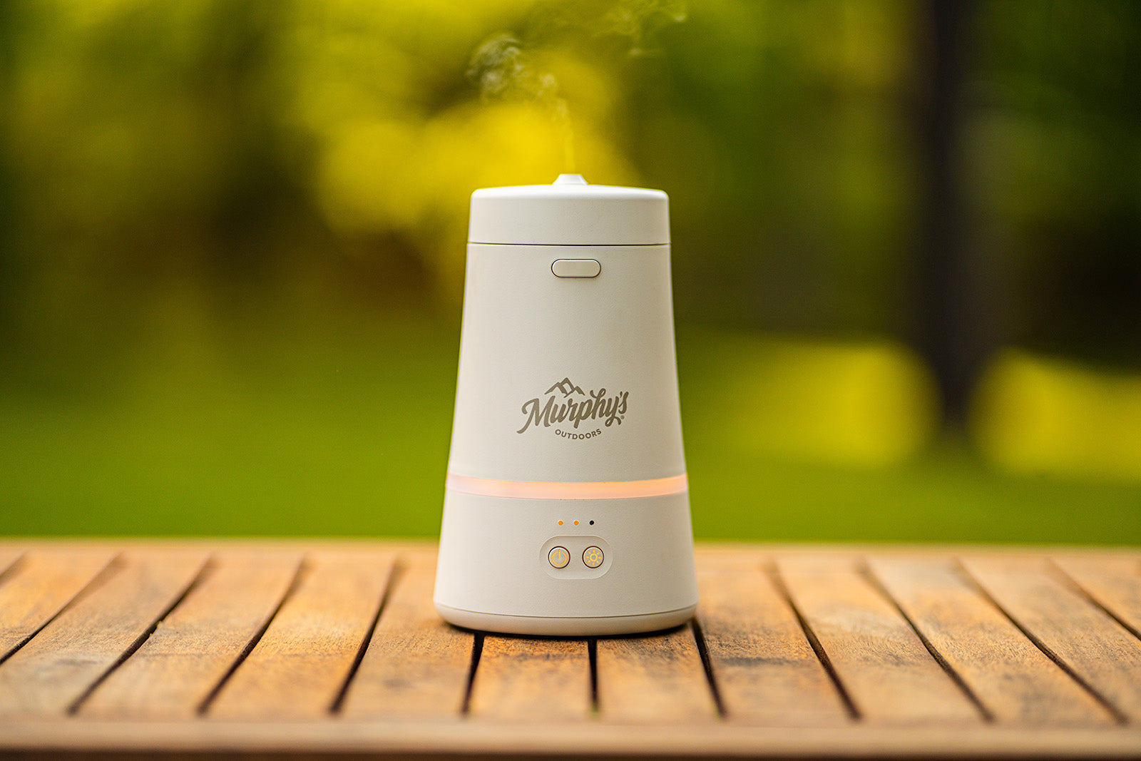 Murphy's Naturals Mosquito Dodger Zone Repellent sitting on a picnic table with a green background. The device is on and emitting a fine mist.